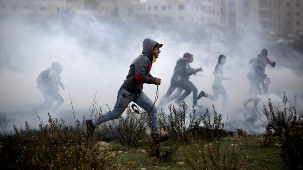 Palestinian protesters run for cover from tear gas fired by Israeli soldiers during clashes in Ramallah on Monday. 