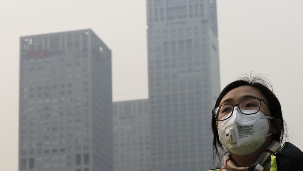 A woman wearing a face mask to protect herself from pollutants walks past office buildings shrouded with pollution haze in Beijing last December. 