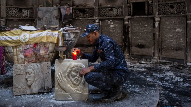 A member of the Iraqi federal police lights a candle inside a church burned and destroyed by Islamic State during their occupation of the predominantly Christian town of Qaraqosh.