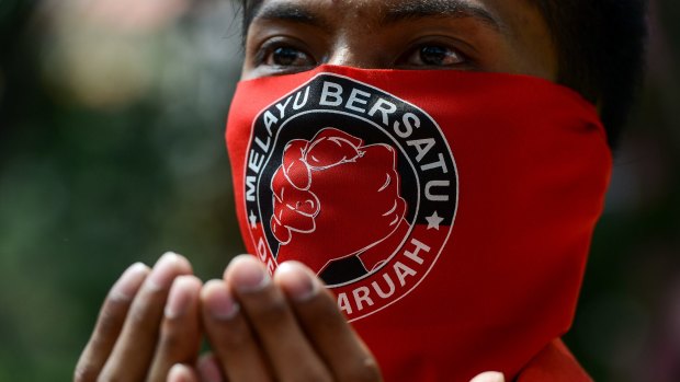A pro-government 'red shirt' protester prays with a face mask emblazoned with the "Malay United" slogan at the pro-government demonstration in Kuala Lumpur on Wednesday. 