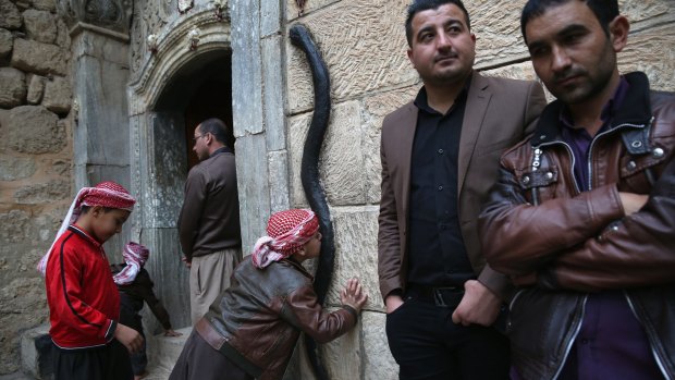 A Yazidi boy kisses a figure of a black snake at the entrance of the Temple of Lalish,in Nineveh Province, Iraq. 