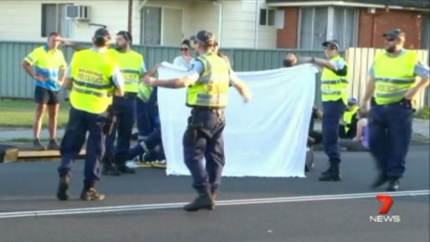 Police hold up a sheet while the woman is treated on the road.