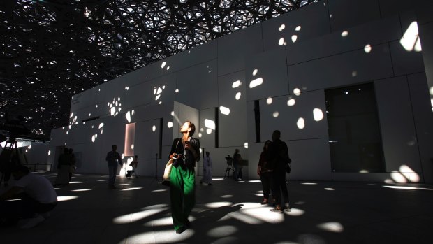 A journalist walks under the lights coming through of the dome at the Louvre Abu Dhabi, UAE, before its Saturday grand opening to the public. 