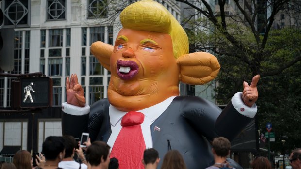 An inflatable caricature of President Donald Trump rises above pedestrians at W. 59th Street and 5th Ave., in New York on Monday.
