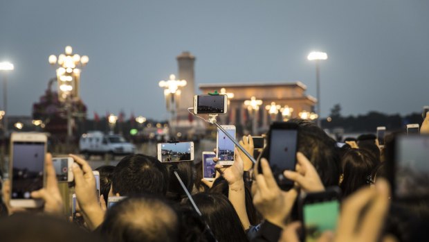 Visitors use smartphones to take photographs and videos of a flag lowering ceremony at Tiananmen Square on Monday.