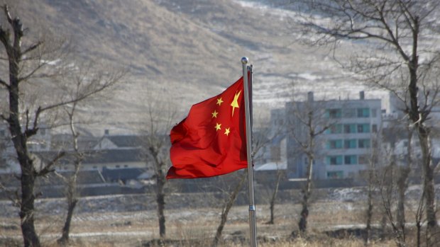 China's national flag flutters on the Chinese side of the banks of the Tumen river, as a North Korean village is seen behind.