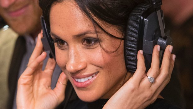 Meghan Markle smiles as she listens to a broadcast through headphones during a visit to the Reprezent FM.