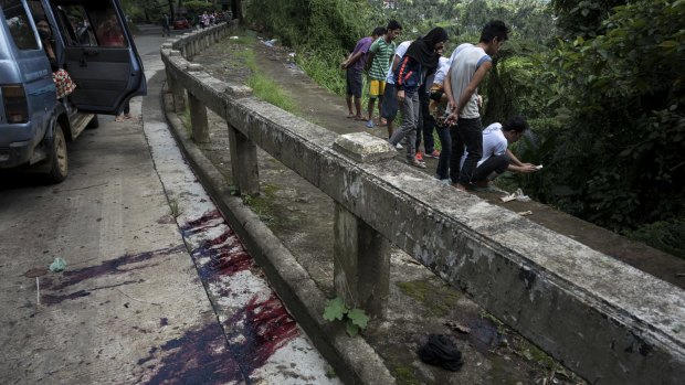 Blood stains the roadside as  civilians view bodies dumped in a ditch by militants. The eight executed men, who were hogtied, had a cardboard sign tied to their bodies bearing the word "munafik", or hypocrite.
