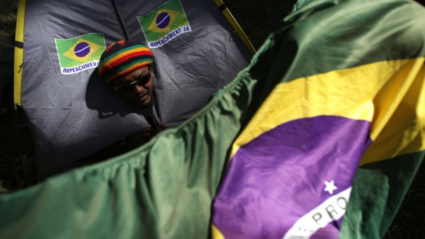 A demonstrator peeks out from his tent, decorated with stickers that say "Impeachment Now".