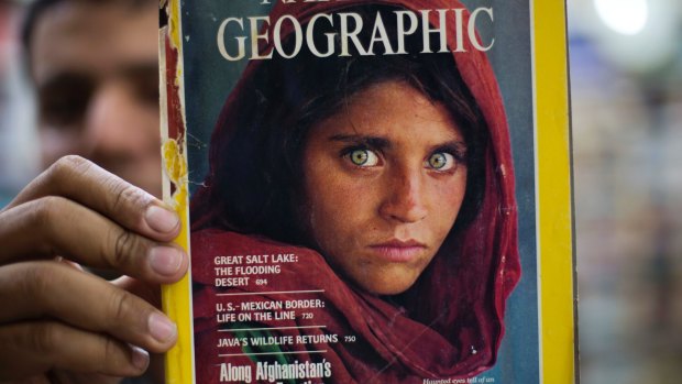 Pakistan's Inam Khan, owner of a book shop, shows a copy of a magazine with the photograph of Afghan refugee woman Sharbat Gula  from his  collection in Islamabad, Pakistan.