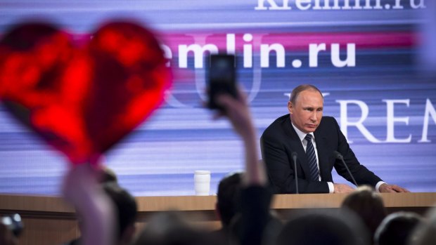 Russian President Vladimir Putin speaks at his annual end of year news conference in Moscow on Thursday as  a reporter holds up a heart-shaped poster to attract his attention.