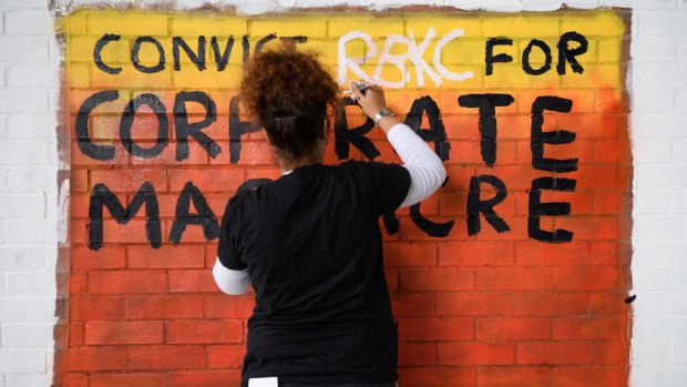 A woman paints a sign calling for the conviction of Kensington and Chelsea Council for corporate manslaughter.