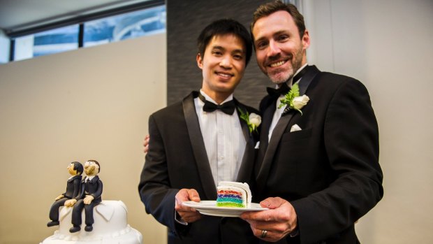 Ivan and Chris Hinton-Teoh hold a slice of their rainbow wedding cake from Erindale Bakery next to the cake toppers made by Nada's Cakes. 
