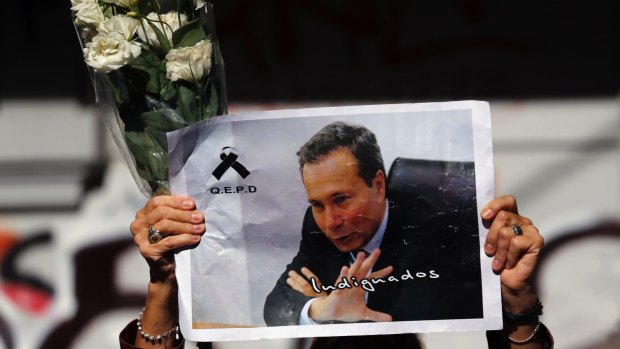 A woman holds up flowers and an image of late prosecutor Alberto Nisman while waiting for the hearse with his remains.