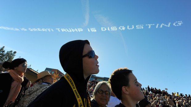 Spectators watch as sky writers write "America is great! Trump is disgusting" above the route of the Rose Parade in Pasadena.
