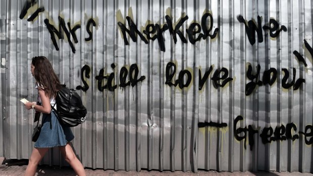 A young woman walks past a graffiti acknowledging Germany's role in propping up Greece.