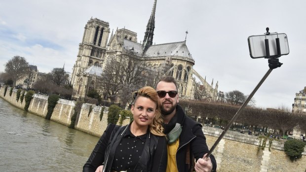 Tourists use a selfie stick to take a photo of themselves near Notre Dame in Paris.