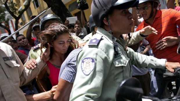 A woman is detained by national police during clashes between supporters of jailed opposition leader Leopoldo Lopez and government loyalists outside the courthouse in Caracas, Venezuela.