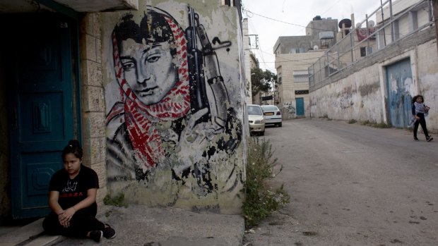 A Palestinian girl sits beside a mural of Palestinian militant Leila Khaled at the entrance of her family's home in the Aida refugee camp, ahead of the funeral procession of 13-year-old  Abdel Rahman Shadi.
