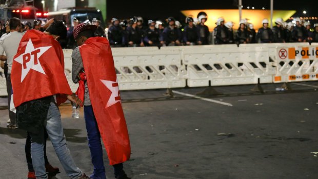 Pro- Rousseff supporters stand draped in flags in front of heavy police presence outside the Congress in Brasilia on Wednesday,