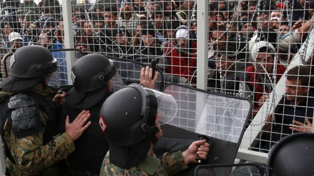 Stranded refugees and migrants try to break an iron fence from the Greek side of the border as Macedonian policemen push them back, near Gevgelija on Monday.