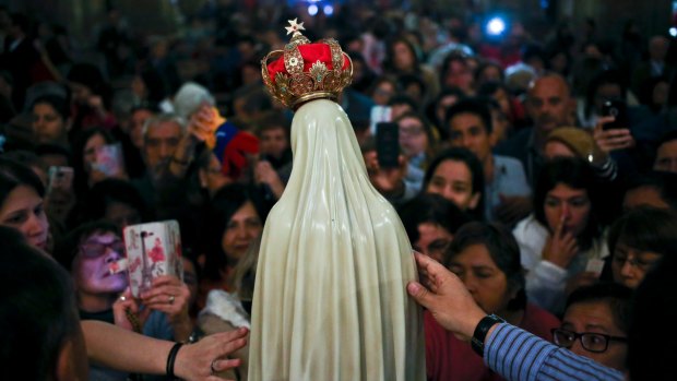 Believers reach out to touch a statue of Our Lady of Fatima after a Mass in her honour at the Metropolitan Cathedral in Santiago, Chile,  on Saturday, the 100th anniversary of the vision. 