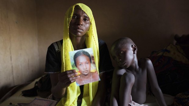 Rachel Daniel, 35, holds up a picture of her abducted daughter Rose Daniel, 17, with her son Bukar, 7.