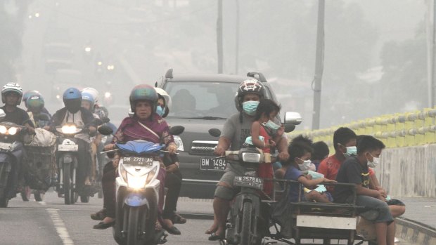 Motorists ride on a road as thick haze from wildfires blankets the city of Pekanbaru, Riau province.