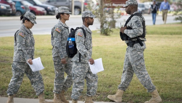 Soldiers walk past a military police officer, right, patrolling the perimeter of the US Army IMCOM HQ on Thursday, before the hearing to determine if  Bowe Bergdahl will be court martialed.