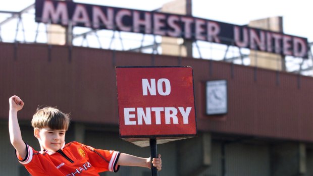 A young Manchester United fan hung from a "no entry" sign at the football club's home stadion after the British government blocked BSkyB's $1 billion takeover bid.