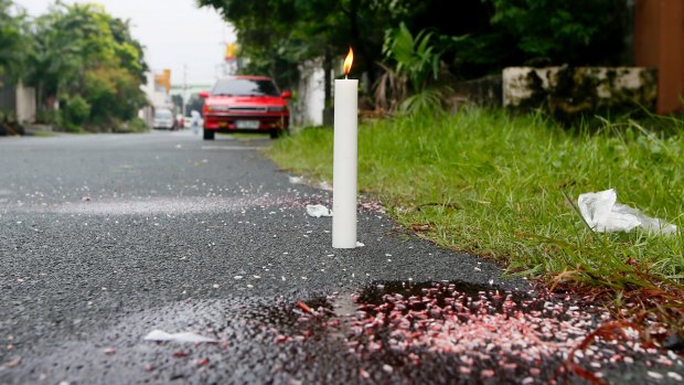 A candle marks the spot where three bodies were dumped by unknown men along a secluded street in suburban Quezon City north-east of Manila.