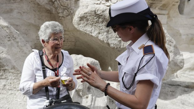 A city police officer talks to a woman having an ice-cream by the Trevi fountain. City authorities are cracking down on eating snacks in public places 
