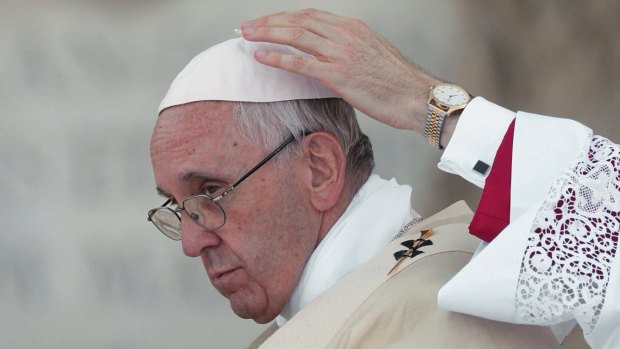 A master of ceremonies adjusts Pope Francis' skull-cap during a Mass in June