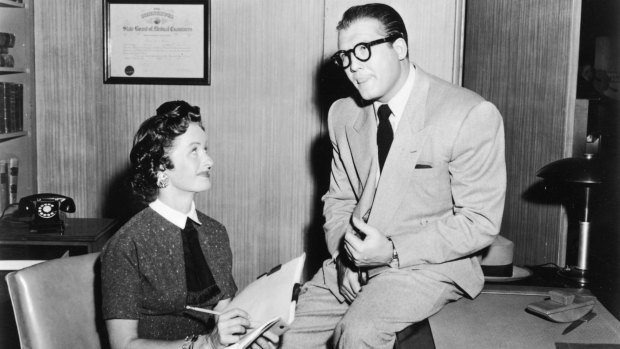 American actor George Reeves (1914 - 1959), as Clark Kent, sits on desk beside Noel Neill, as Lois Lane, in a still from the television series, Adventures of Superman (1955).