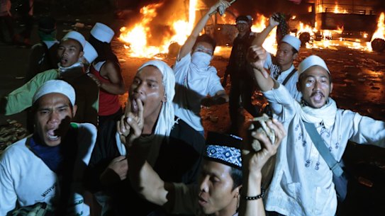 Muslim protesters chant slogans near burning police trucks.