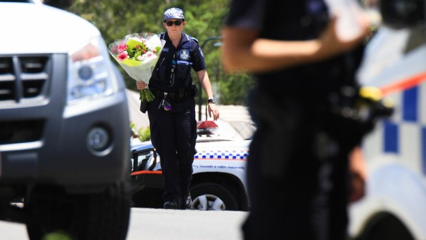 A police officer takes flowers delivered by a neighbour to the scene where Ms Bradford and her estranged husband's bodies were found.