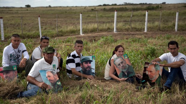Residents display pictures of Fidel Castro as they sit on the shoulder of a countryside road waiting for the military jeep carrying his ashes.