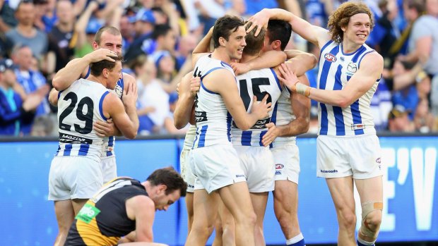 Roo huddle: North Melbourne players celebrate while Tiger Jake Batchelor sinks to the ground.