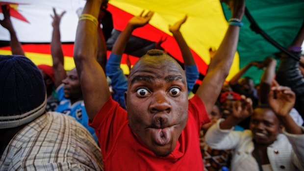 A happy protester stands under a large national flag, at a demonstration of tens of thousands at Zimbabwe Grounds in Harare, Zimbabwe.