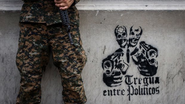 A soldier stands next to a stenciled graffiti that reads in Spanish "Truce between politicians" painted on the main walls of the National Palace in San Salvador, El Salvador. 
