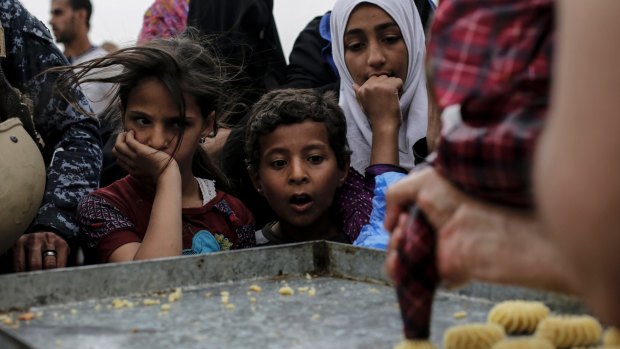 Children stare at a baker baking fresh cookies at a food distribution point in western Mosul, Iraq. Thousands of people still live in the western part of the city where food is getting scarce due to fighting between Iraqi forces and the Islamic State group.