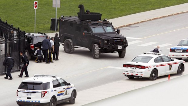 Police officers take cover near Parliament Hill following the shooting incident in Ottawa.