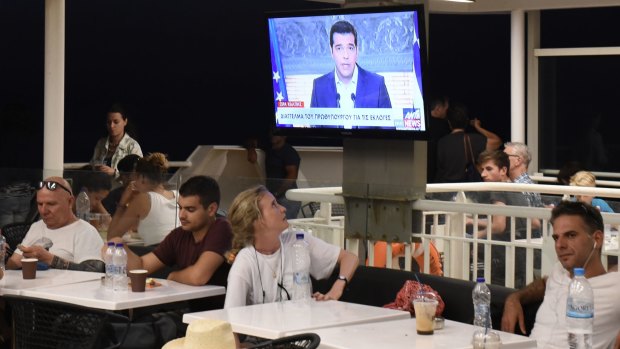 Greek Prime Minister Alexis Tsipras, announces his resignation on TV, watched by a tourist on a ferry in the Aegean sea.