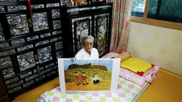 Former South Korean 'comfort woman' Kim Bok-dong poses with a copy of her painting titled 'The Day A 14-year-old Girl Is Stolen Away' in Seoul. According to her testimony, she was forced to have sex with at least 15 Japanese soldiers each day during World War II.