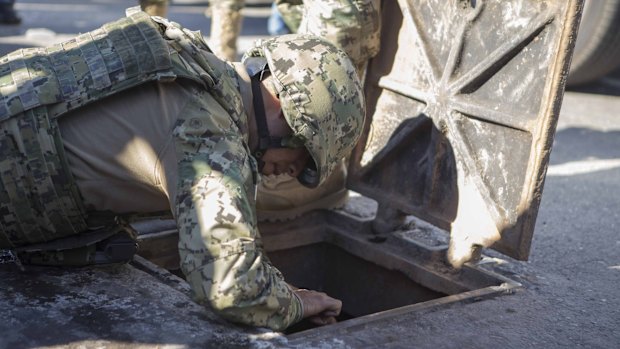 A Mexican marine inspects a manhole where high-powered weapons were found to be abandoned, in the neighbourhood where drug lord Joaquin Guzman Loera was found.