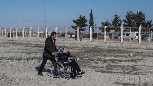 A man pushes a woman in a wheelchair towards the entrance of the Kilis refugee camp at the closed Turkish border gate on Tuesday.