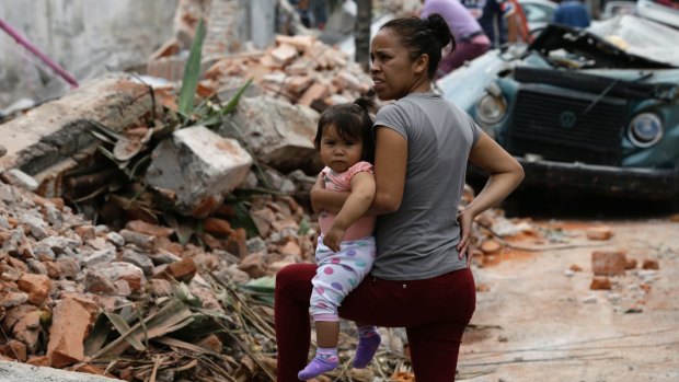 A woman in Mexico City holds her child as she stands next to a wall that turned to rubble during Friday's massive earthquake.