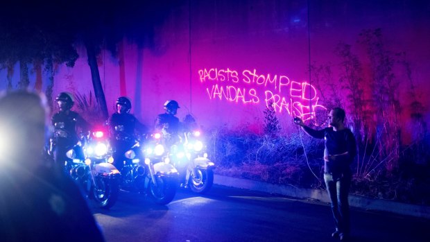 Graffiti spray-painted by a protester lines a wall as police officers clear demonstrators from a freeway off-ramp in Oakland, California on Saturday.