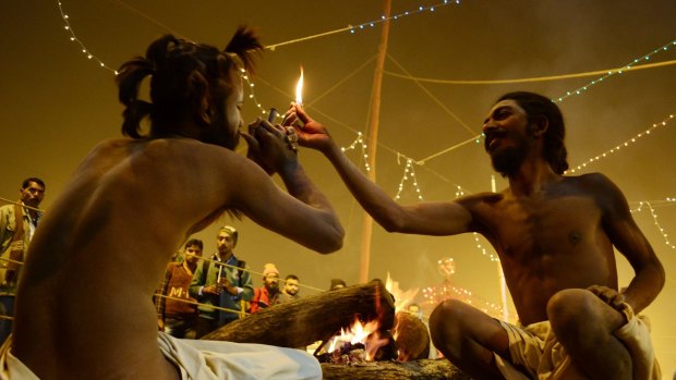  A Naga Sadhu gets ready to smoke a chillum  as another strikes the match to light it  in their camp in the Kumbh Mela area.  