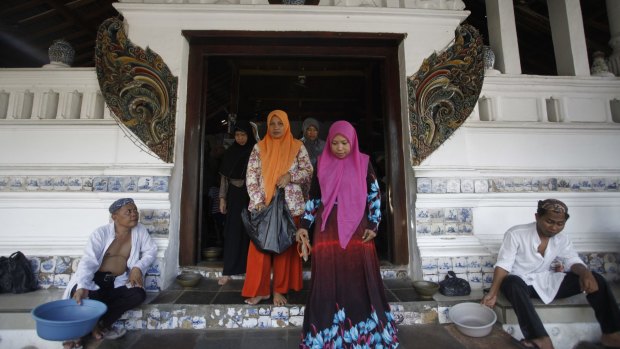 Men hold containers for donations from visiting pilgrims outside the  tomb area.